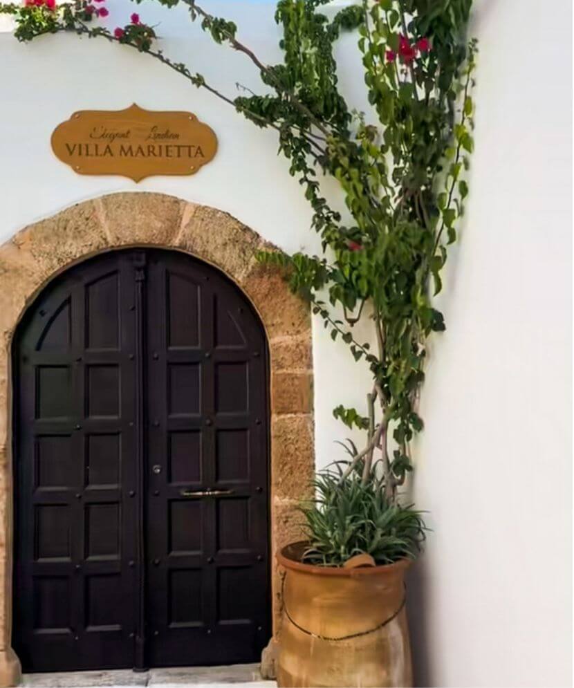 outer facade of a wooden door and tree of a villa marietta in lindos village